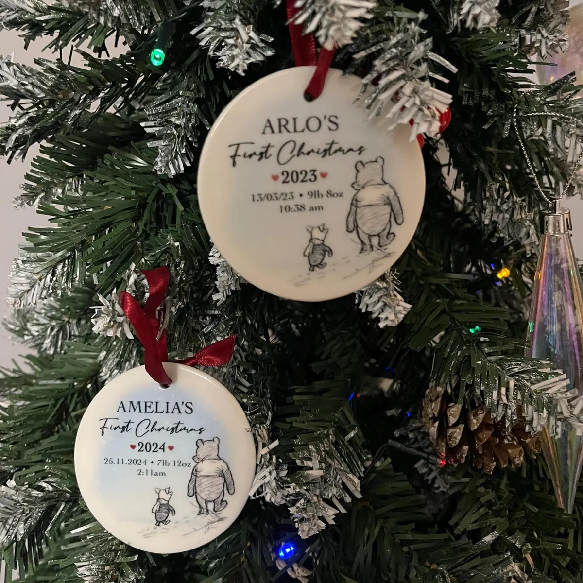 Two Winnie the Pooh first Christmas ceramic baubles for Arlo and Amelia hanging on a tree